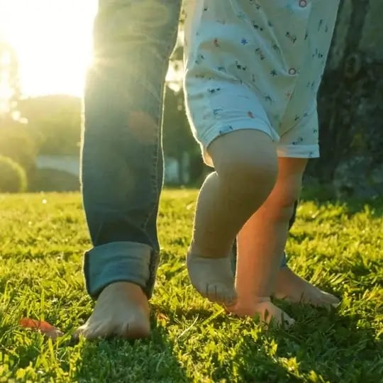 mom and child walking in green grass